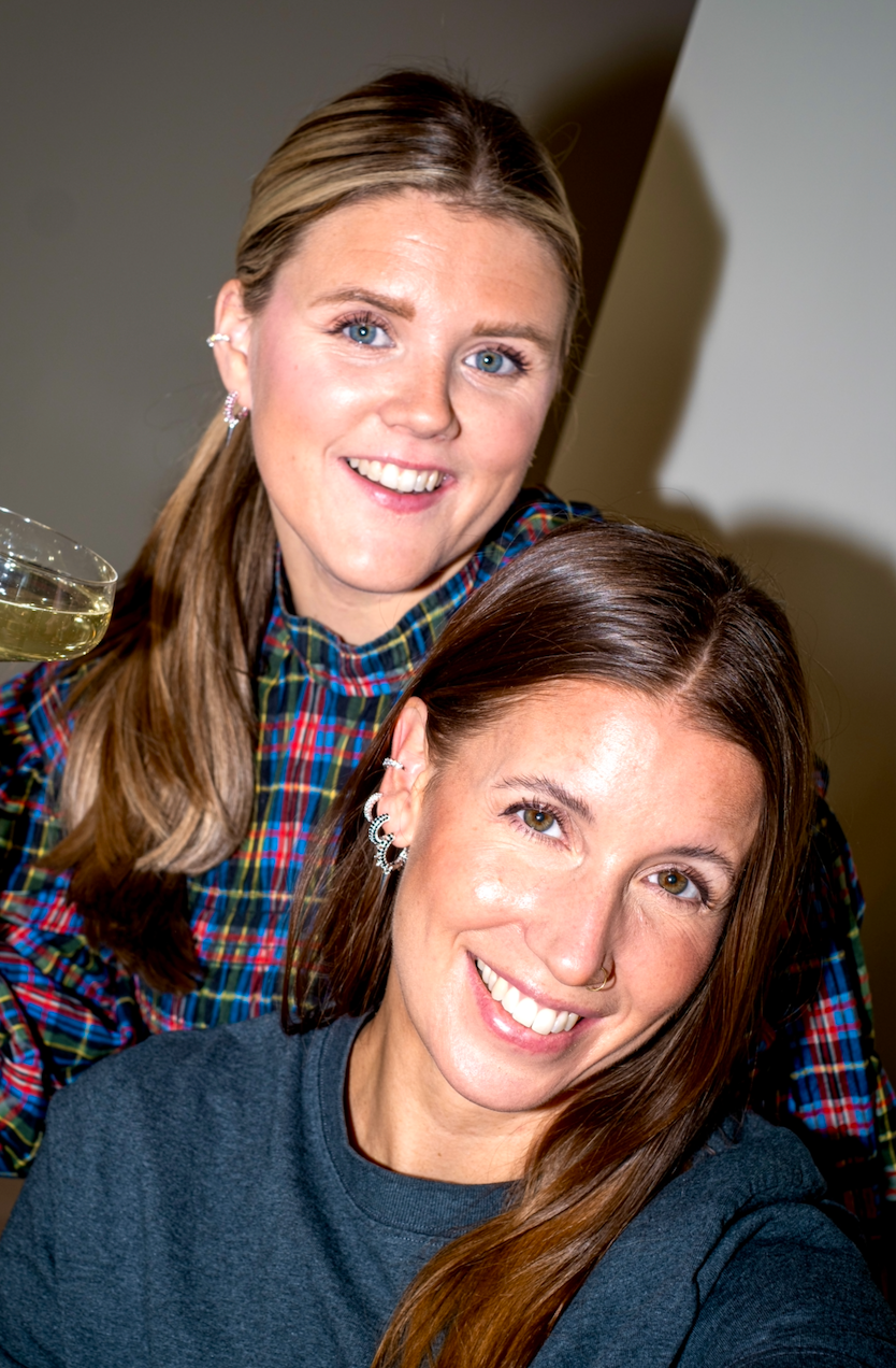 Närbild på två modeller, en brunett och en blond, i festlig stämning. Bär örhängen i olika färger från Studio W