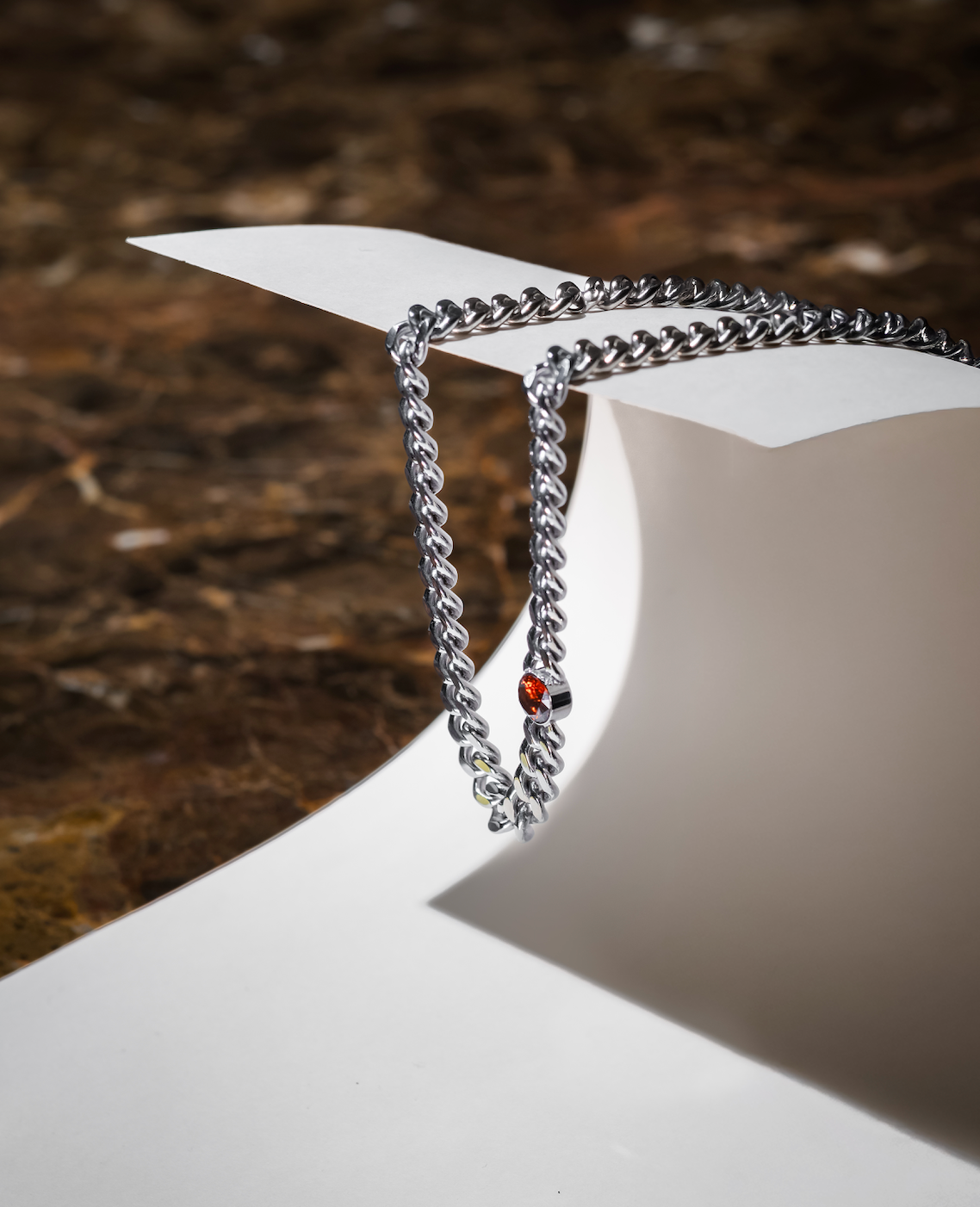 Silverfärgat kedjehalsband i rostfritt stål med bärnstensbrun cubic zirconia-sten, hängande på papper
