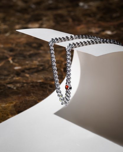 Silverfärgat kedjehalsband i rostfritt stål med bärnstensbrun cubic zirconia-sten, hängande på papper
