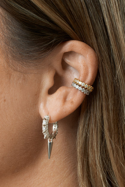 Detaljbild på guld och silver ear cuffs med vita stenar i rad. Hoopörhänge i silver, klätt med klara zirkoner och nitdetaljer. 