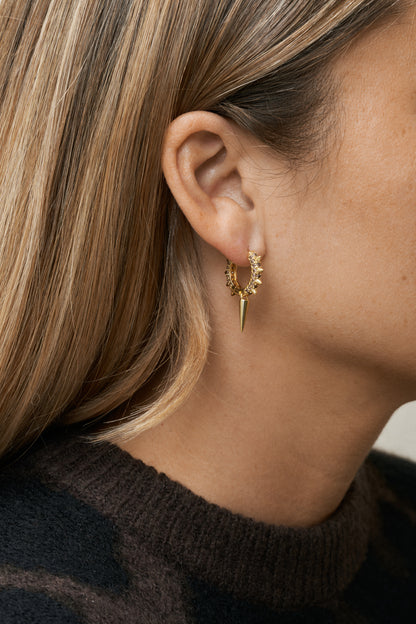 Hoop-örhängen i guld med bruna stenar och edgy siluett. Närbild på öra