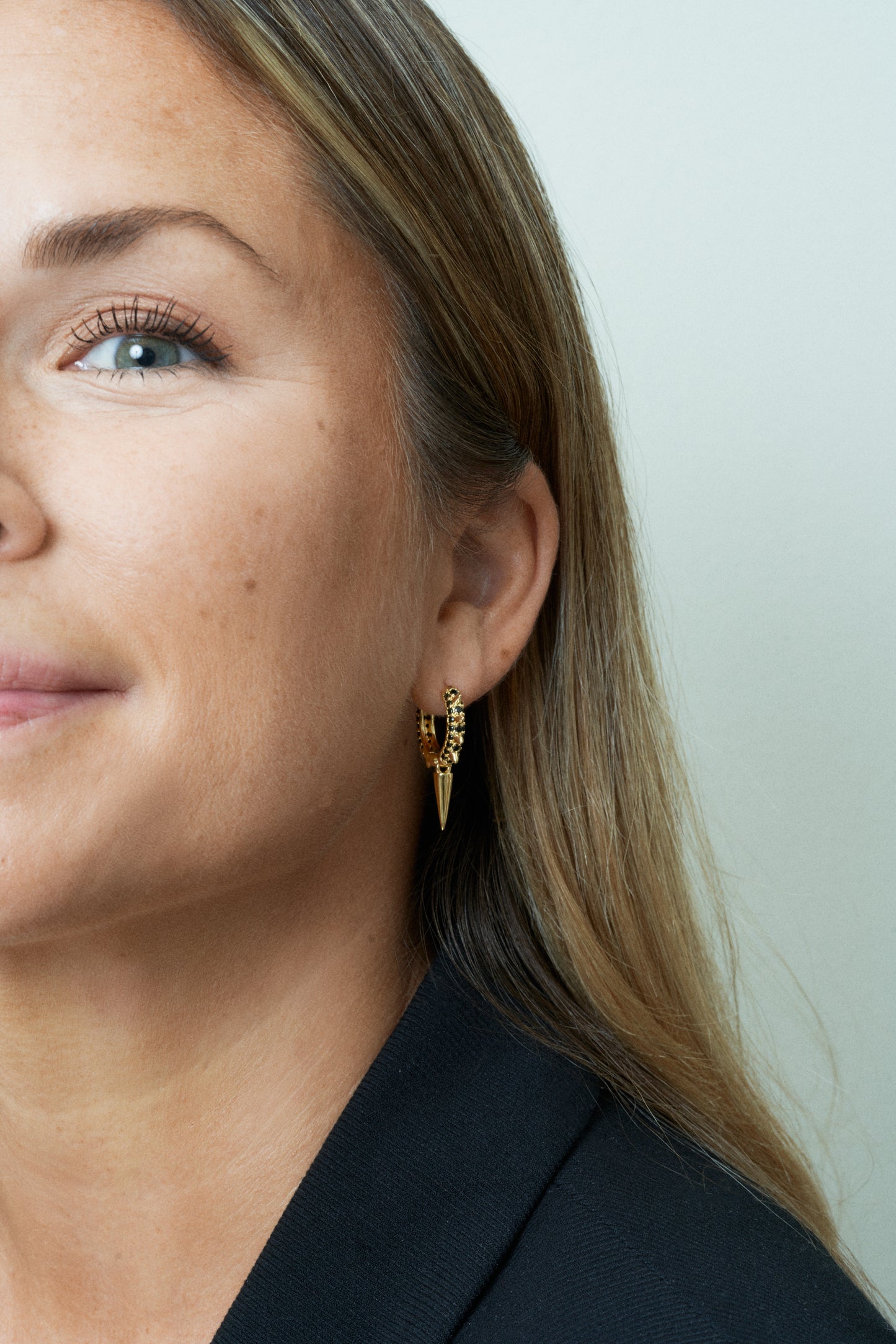 Guld hoop-örhängen med svarta kubiska zirkoner och nitar. Närbild på öra. 