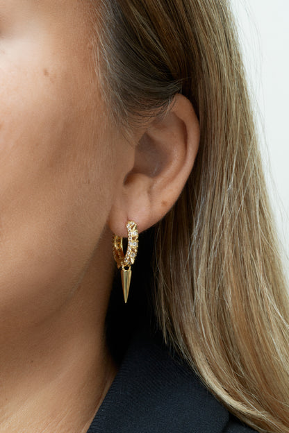 Guldpläterade hoop-örhängen med vita zirkoner och nitar. Närbild på öra