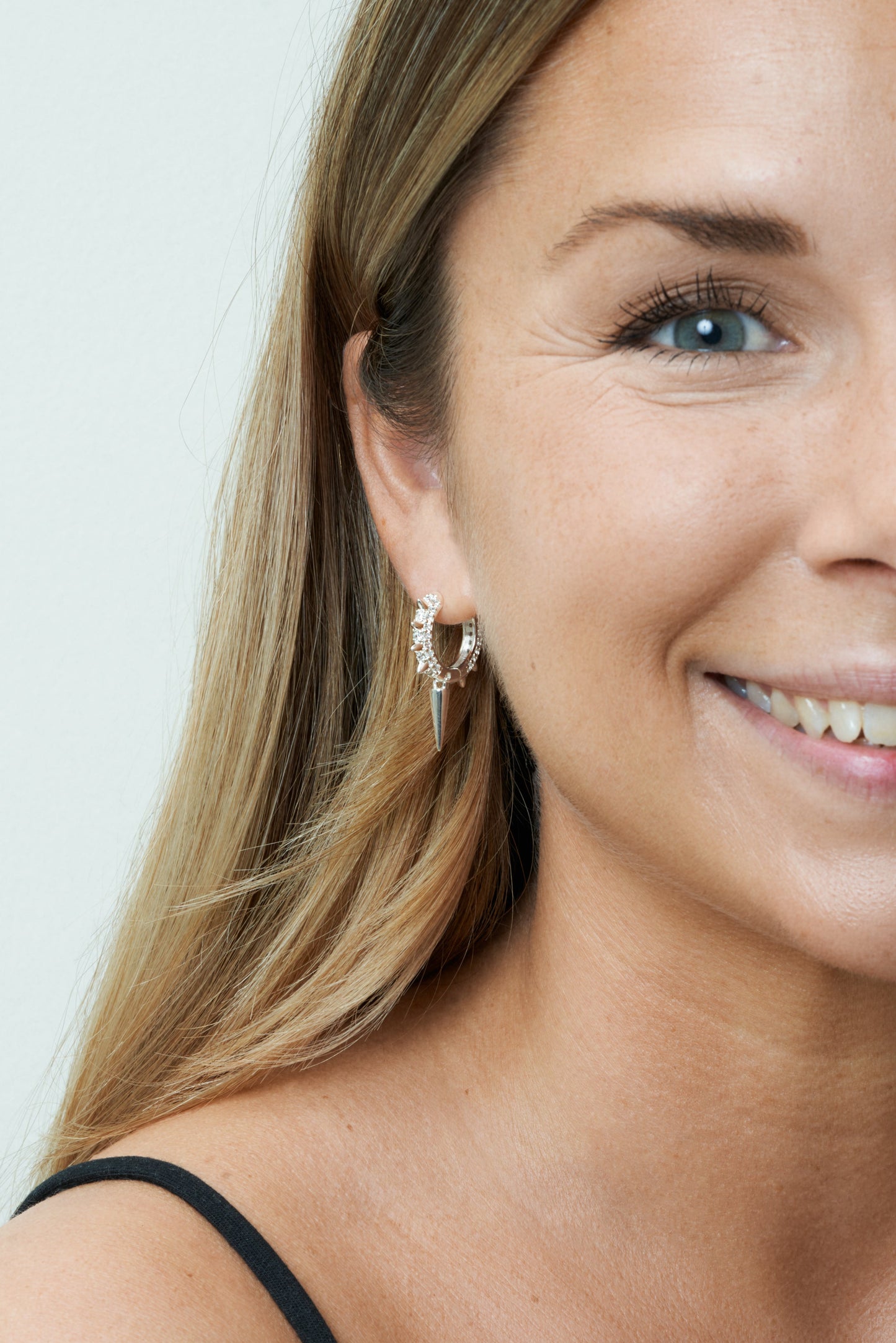 Silver hoops med vita kubiska zirkoner, elegant textur och minimalistisk design. Närbild på modell framifrån