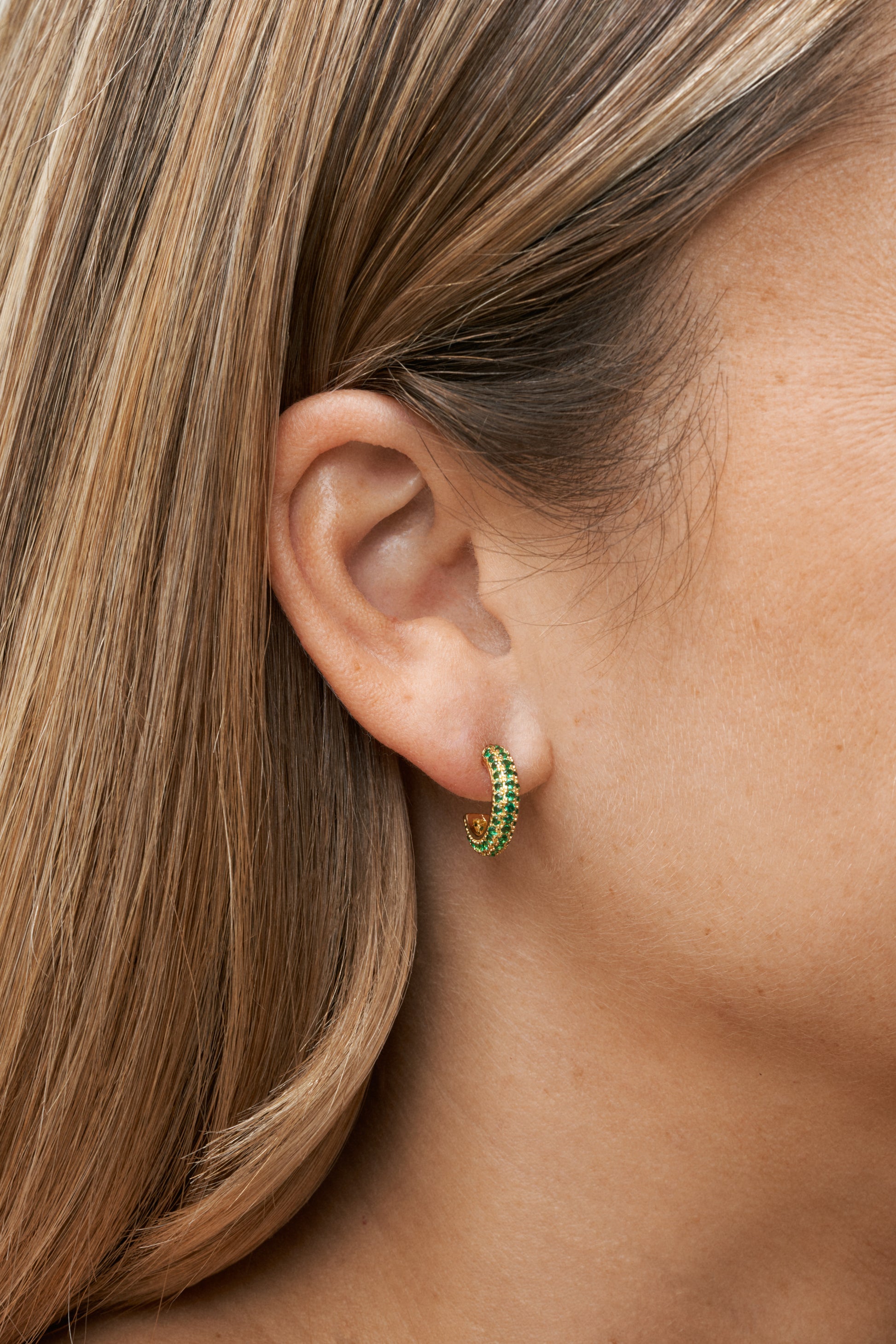 Hoop-örhängen i 18k guldpläterad mässing med gröna zirkonstenar på öra, i närbild