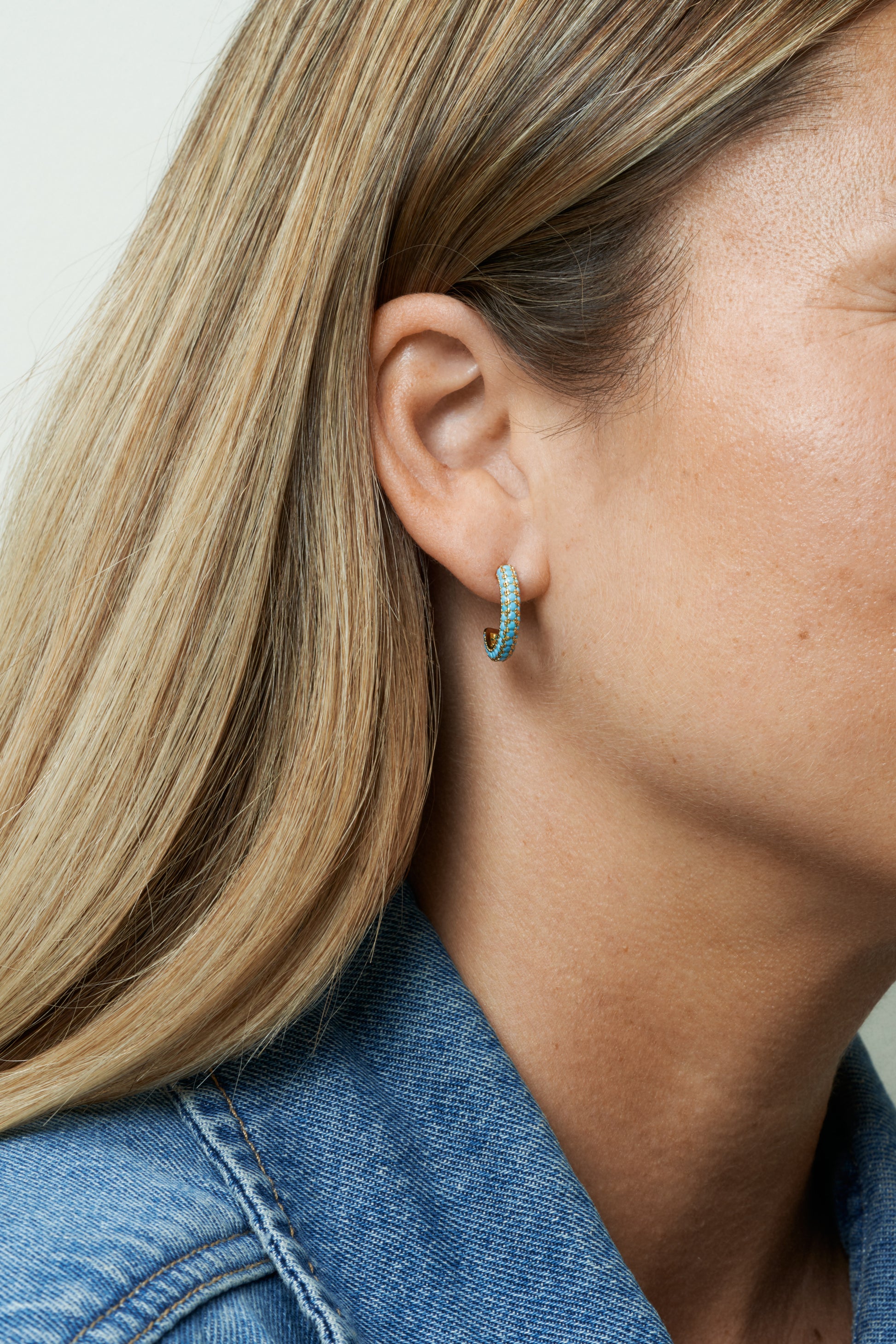 Guldpläterade hoop-örhängen med turkosa stenar, lekfull färgklick. Närbild på öra