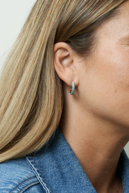 Guldpläterade hoop-örhängen med turkosa stenar, lekfull färgklick. Närbild på öra