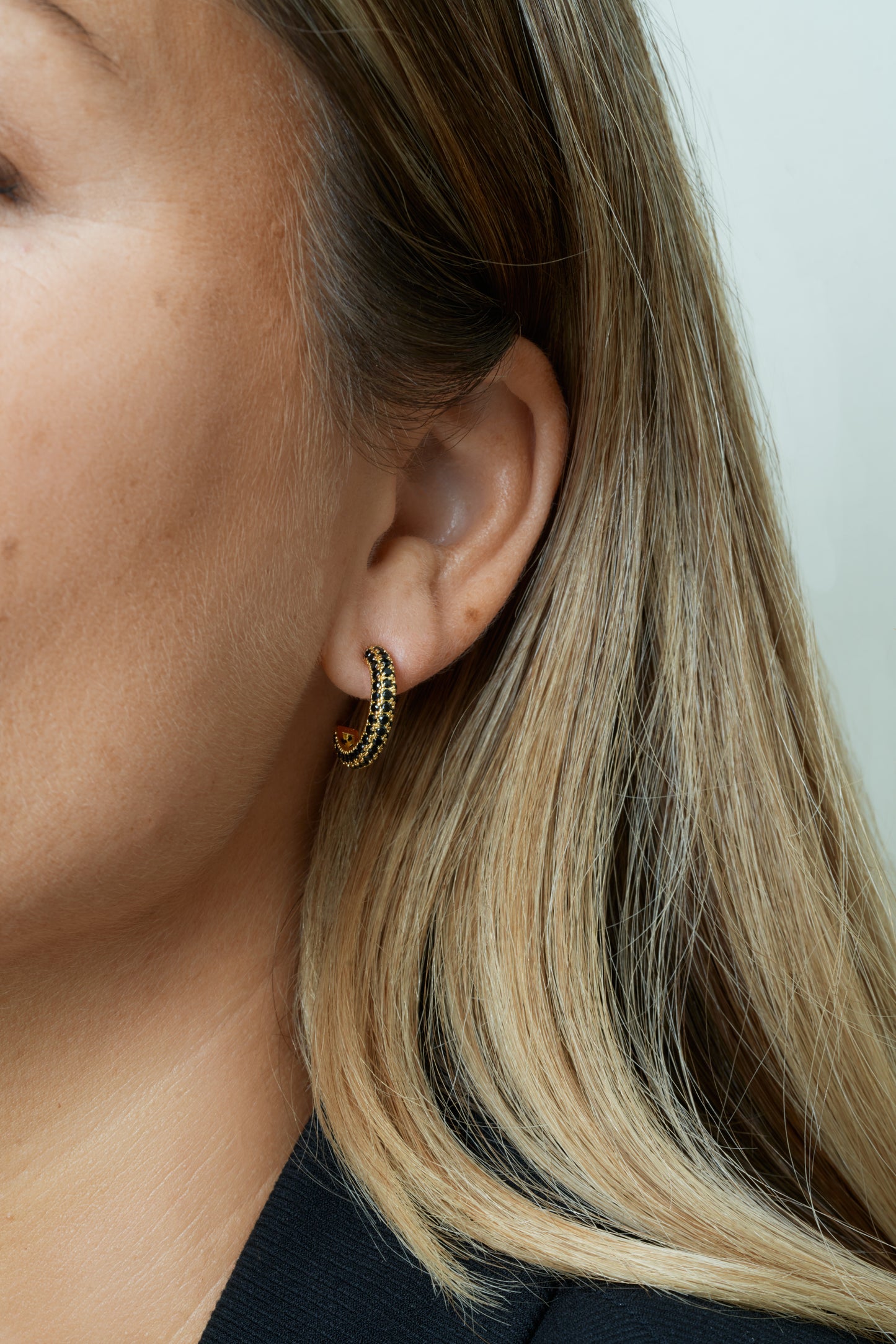 Större hoops i guld med svarta kubiska zirkoner – stilrent och modernt. Närbild på öra