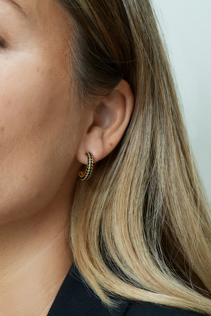 Större hoops i guld med svarta kubiska zirkoner – stilrent och modernt. Närbild på öra