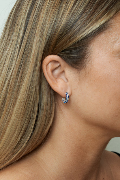 Små silver hoops med blå stenar, stilrena och glänsande. Närbild på öra