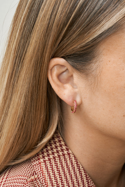 Små guld hoops med röda kubiska zirkoner, på öra i närbild