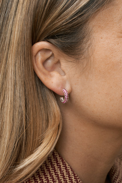Små silver hoops med röda stenar, diskret men färgstark accent. Närbild på öra